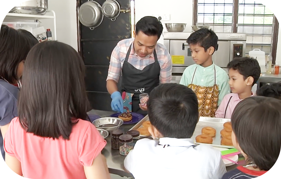 Chef Kecik Rahmat Bahaudin is demonstrating to the children how to make doughnuts at the kitchen.